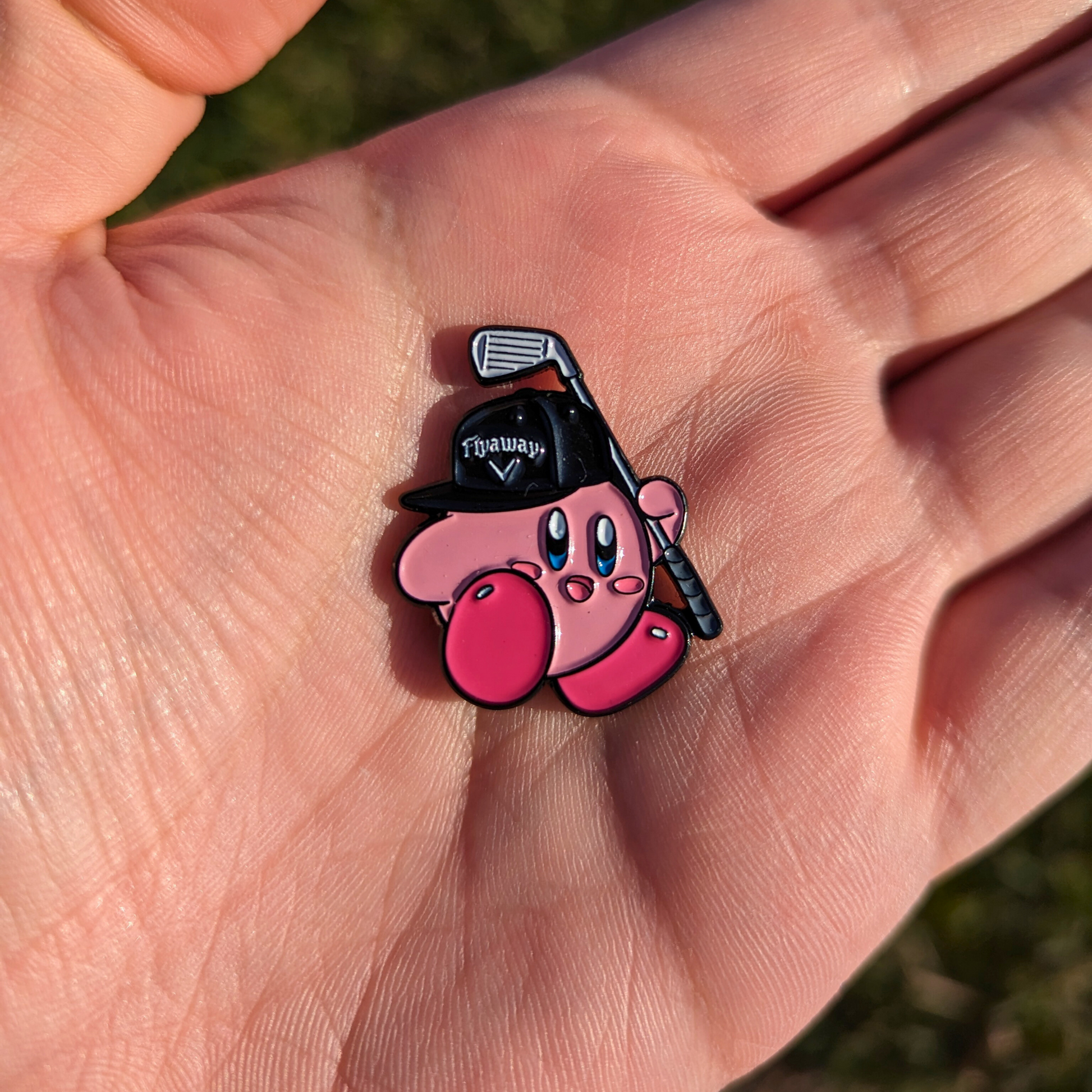 pink kirby video game character wearing flyaway hat and holding golf club golf ball marker in hand