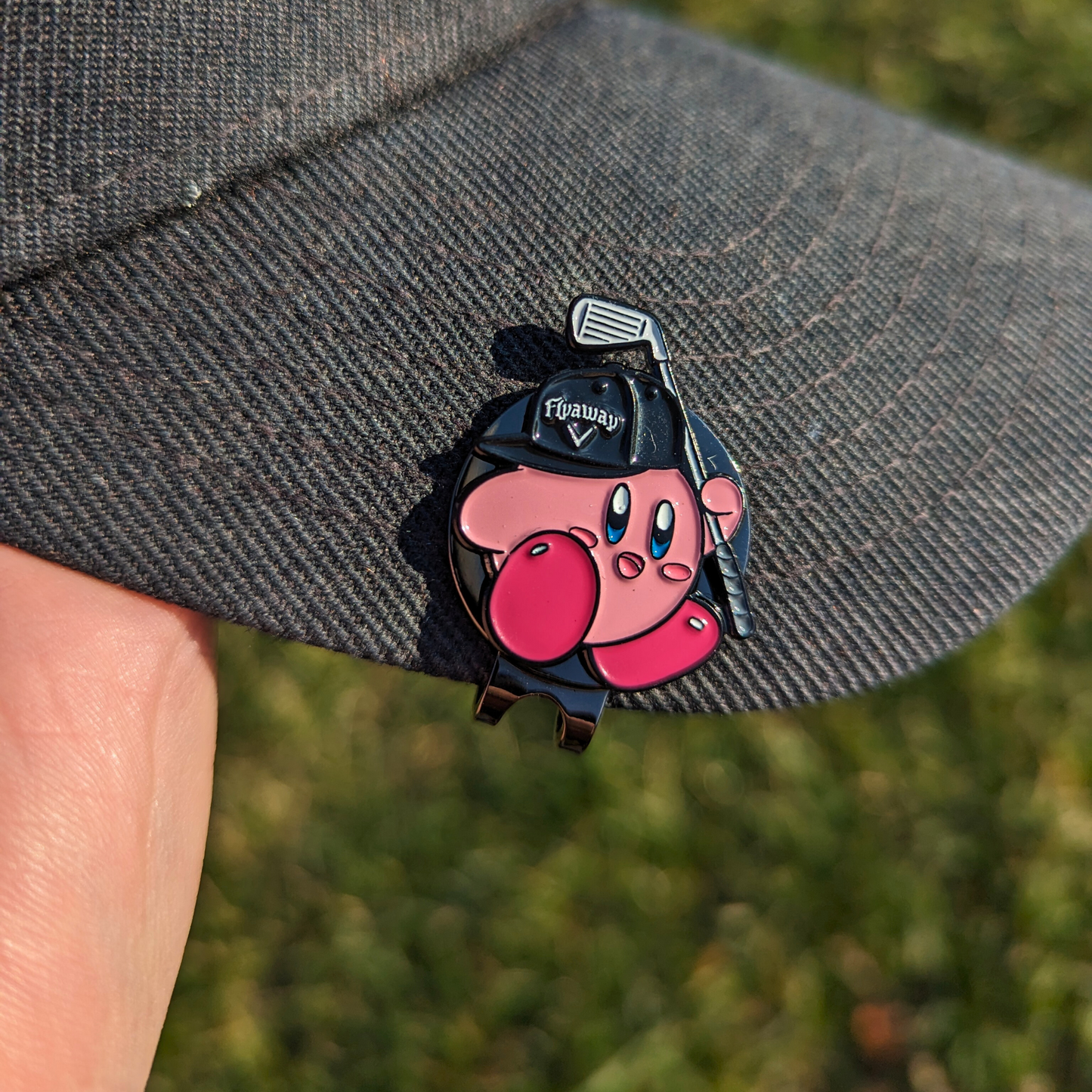 pink kirby video game character wearing flyaway hat and holding golf club golf ball marker clipped to hat
