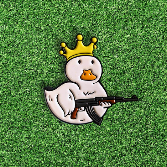golf ball marker of a white duck wearing a gold crown and holding a gun
