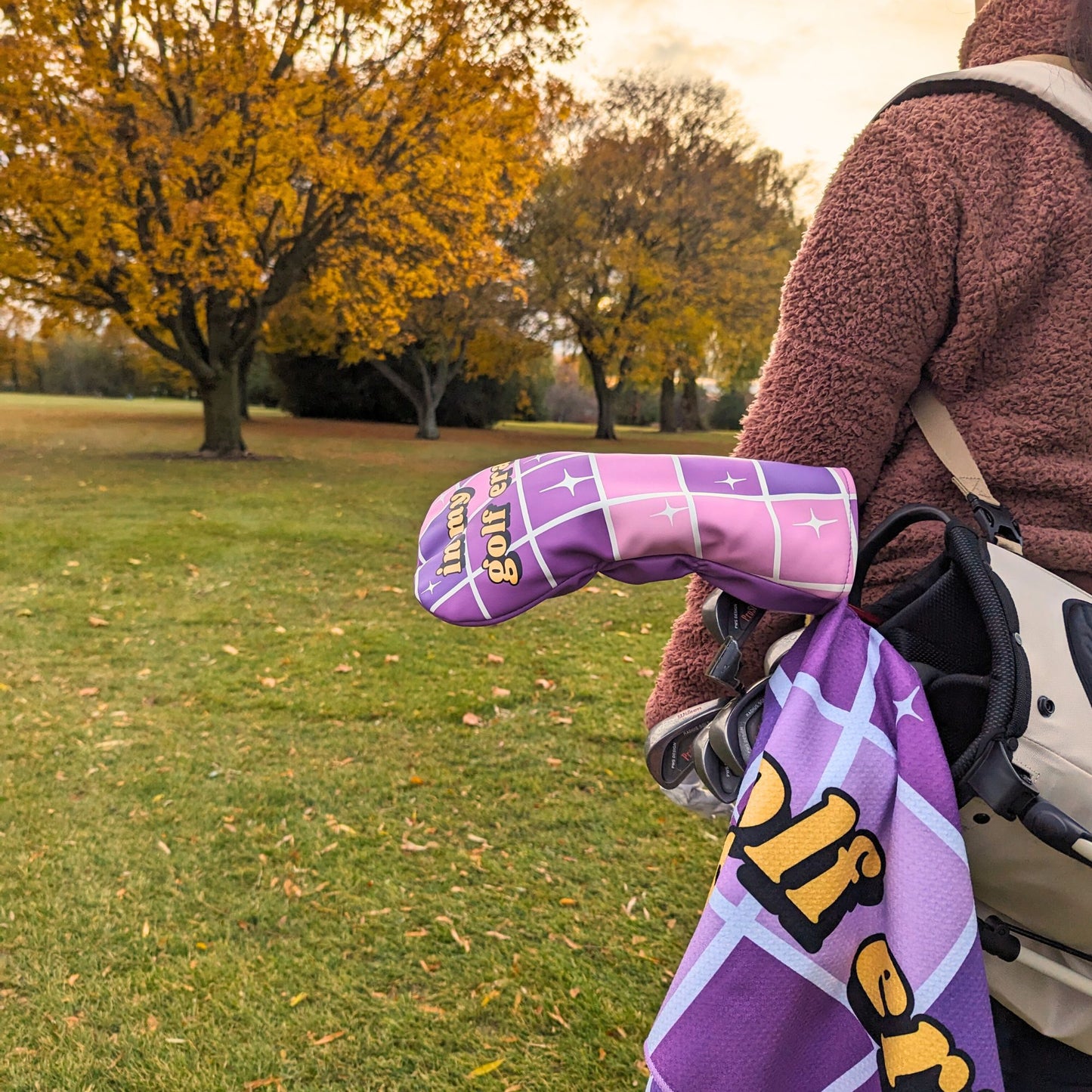 woman holding a golf bag with a purple headcover and towel that say 'in my golf era' with disco ball design