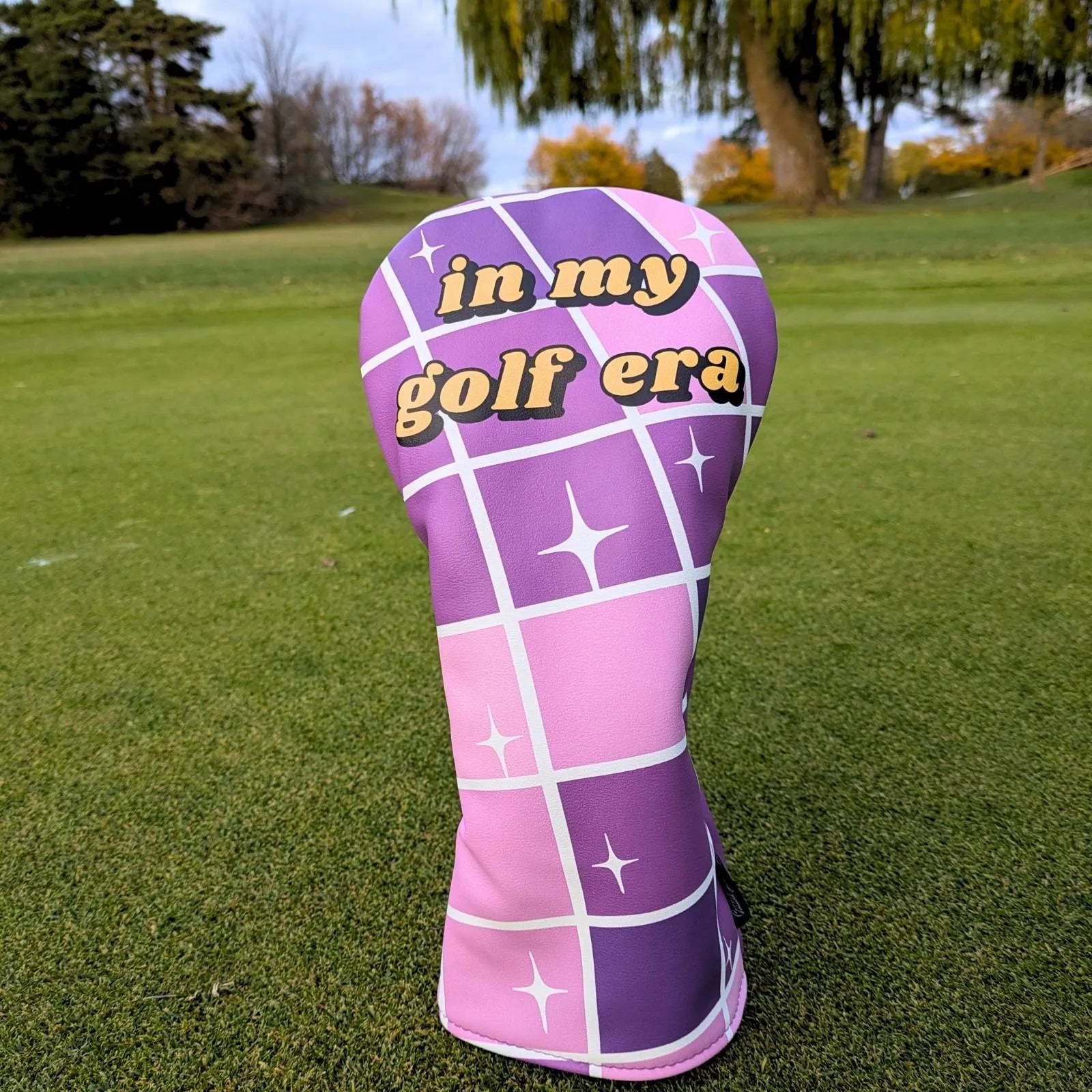 Purple and pink golf club head cover with 'in my golf era' text on a grassy background