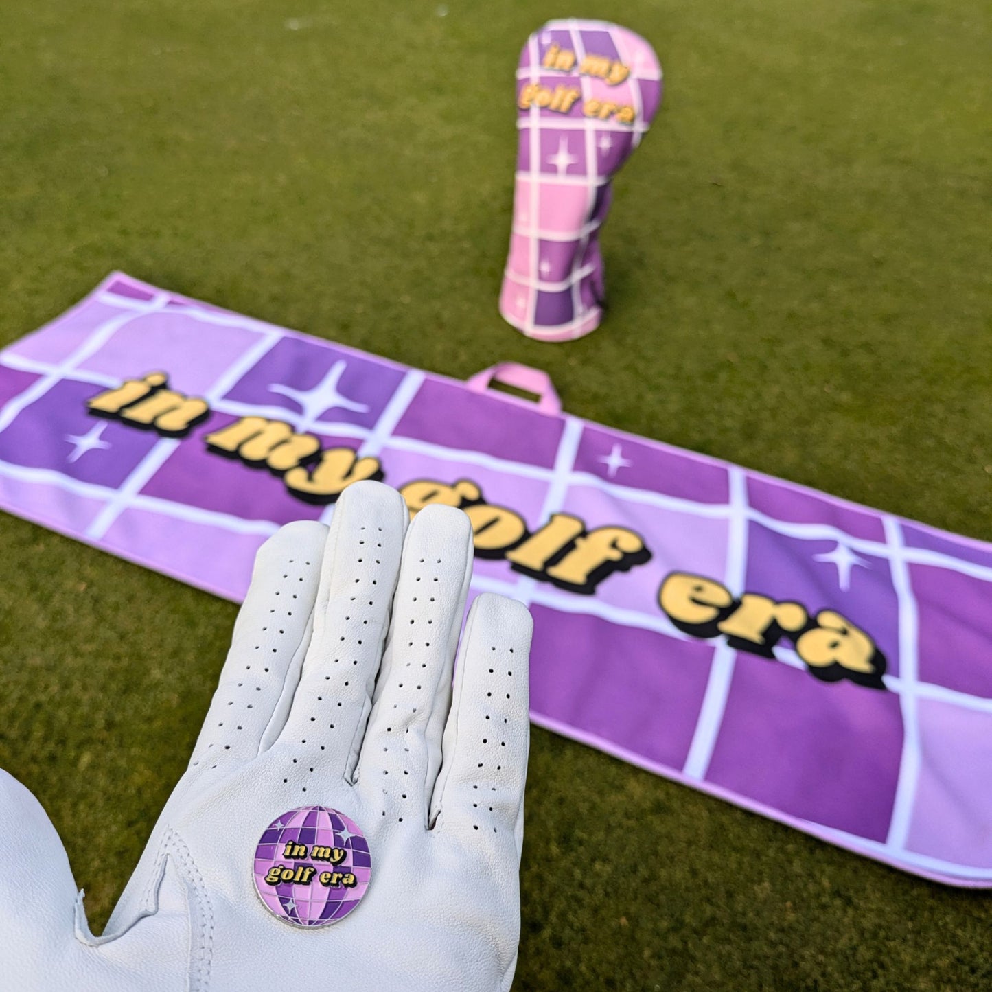 Swiftie golf ball marker, club head cover, and towel with 'in my golf era' branding on a grassy background.